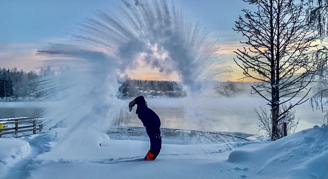 Mies heittää kuumaa vettä ilmaan talven pakkasilla Häränvirran avantouintipaikan luona.