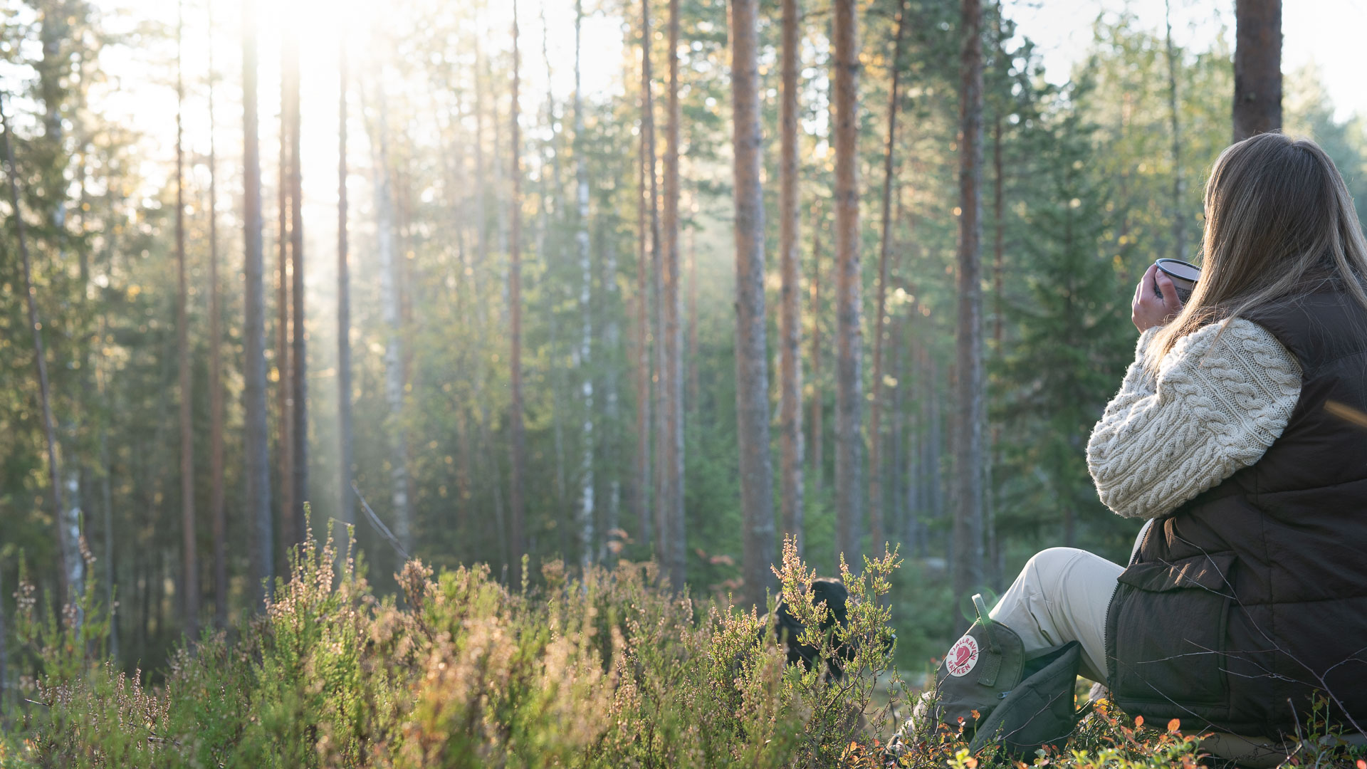 Henkilö istuu metsässä juoden lämmintä.
