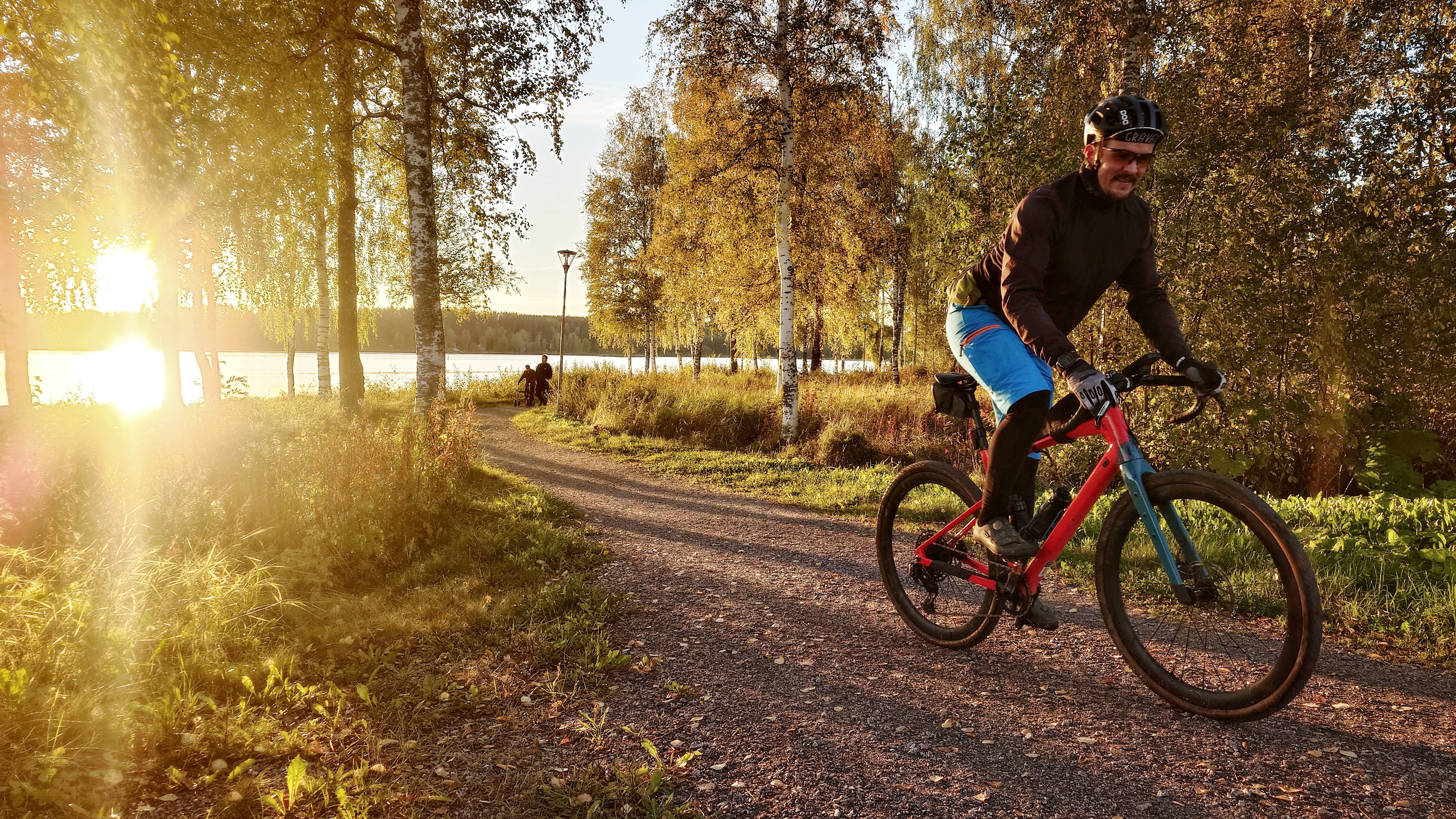 Henkilö pyöräilee rannalla auringon paistaessa takaa. 