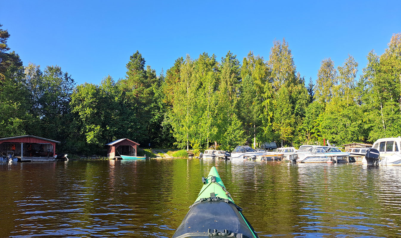 Kajakki on menossa kohti Härkinsalmen satamaa, jossa venevajoja ja veneitä.