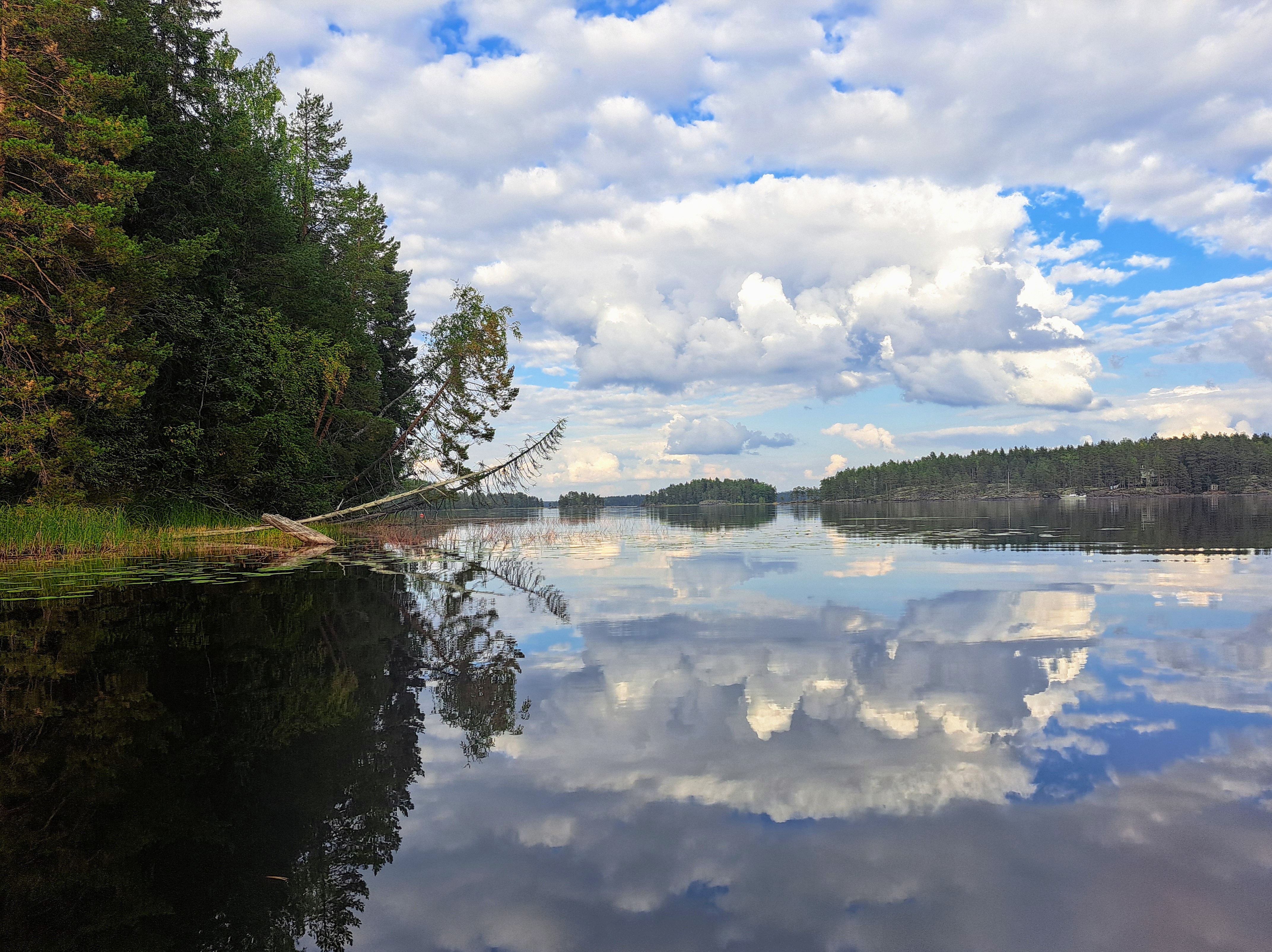Tyyneen järvenpintaan heijastuu pilviä, horisontissa kallioisia saaria.