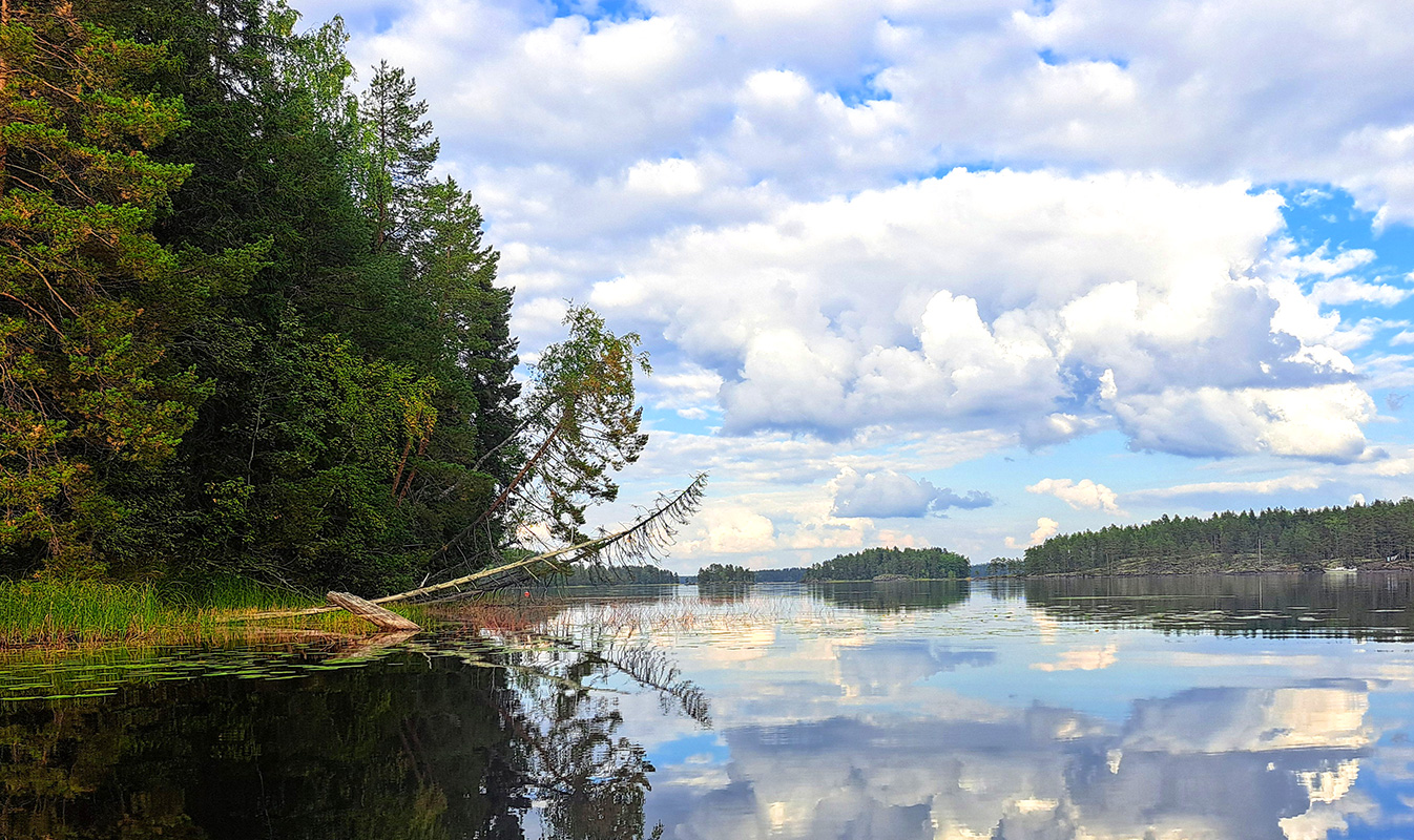 Tyyni järvimaisema, horisontissa kalliosaaria. Pilvinen taivas heijastuu järvenpintaan.