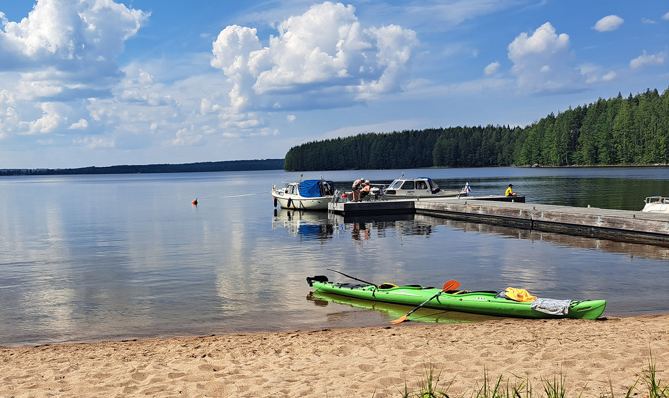Hiekkarannalle on vedetty kanootti laiturin viereen. Laiturilla on kiinnitettynä useampia veneitä.