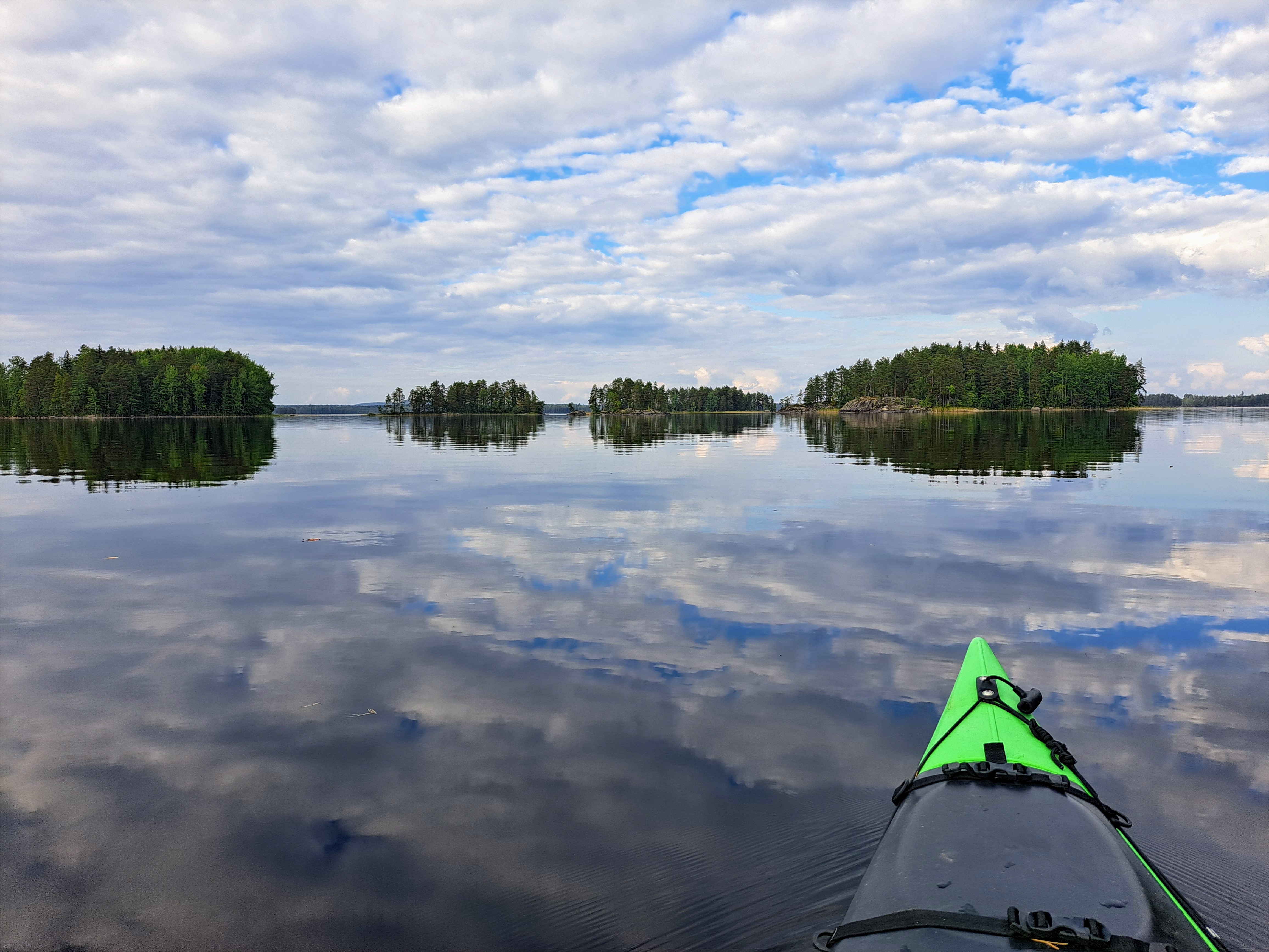 Kuvassa kajakin kärki tyynellä ja pilvisellä järvellä