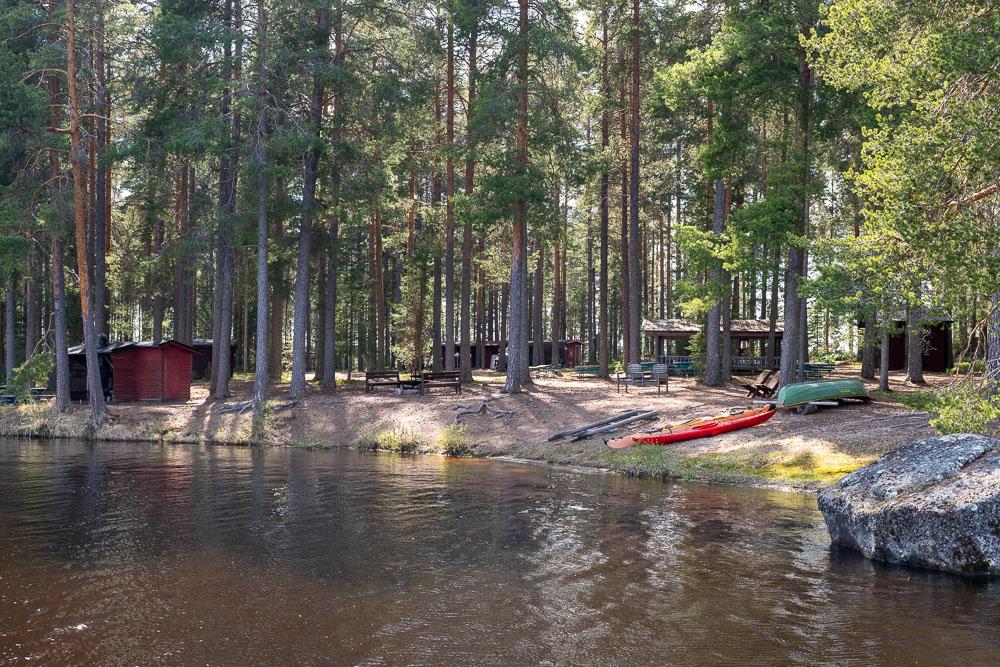 Camping Sumiainen yleiskuva rannasta. Rannassa puustoa, soutuvene ja mökkejä.