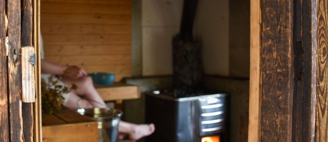 Saunan lauteilla istuu henkilö, kiukaasta hohkaa tuli.