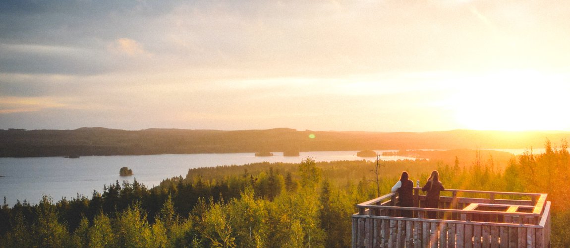 Kaksi henkilöä seisoo Äänemäen näkötornissa ja katsoo auringonnousun värjäämää maisemaa.