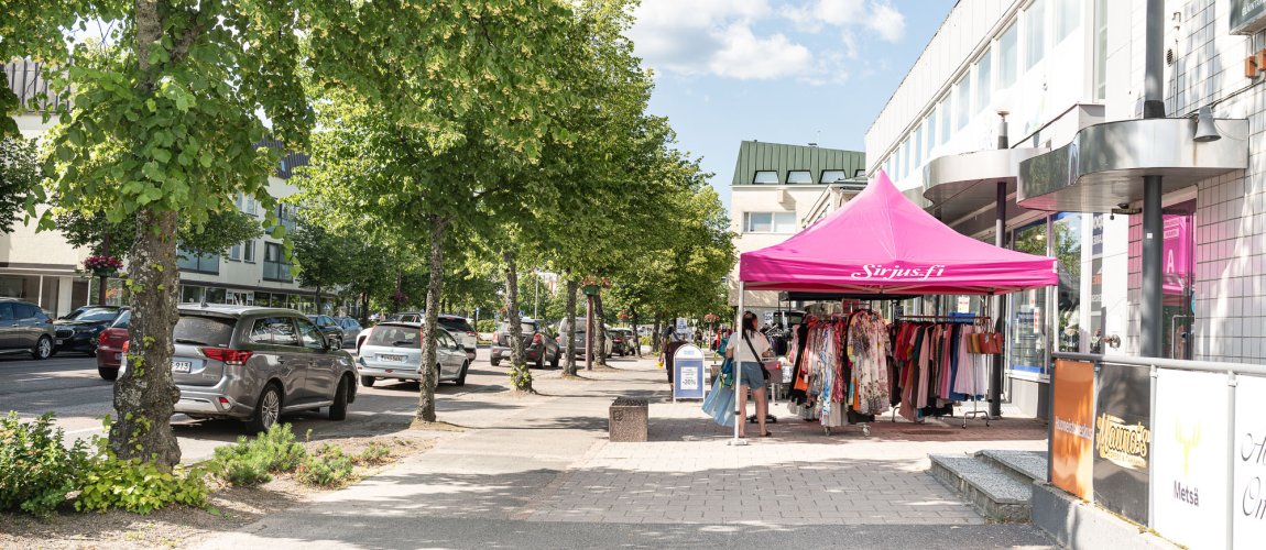 Kesäisellä kadulla pop up -myyntipiste, jossa henkilö katsoo tuotteita.