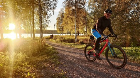Henkilö pyöräilee rannalla auringon paistaessa takaa. 